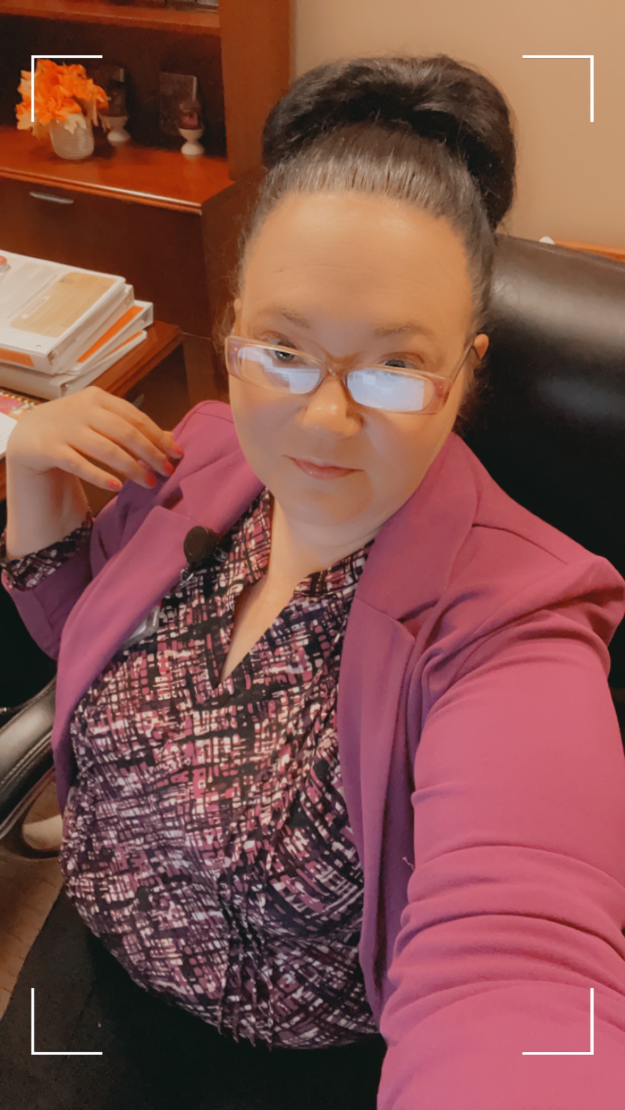 Ashley A. Love smiling in a portrait, wearing a vivid pink blazer and glasses in a warm, cozy room.